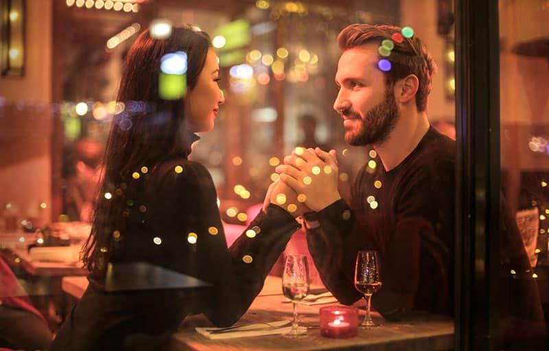 Dating-Paar hält Händchen mit Lichtern, die auf Glas reflektieren