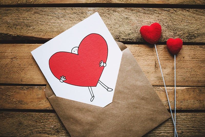 Umschlag mit einer Karte mit einem Herzen, das von einer Figur umarmt wird