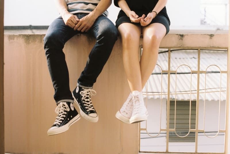 Mann und Frau, die Converse All Star tragen, sitzen auf dem Balkon