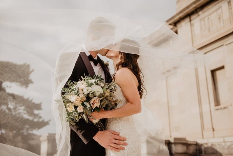 Braut hält Blumenstrauß und küsst den Bräutigam