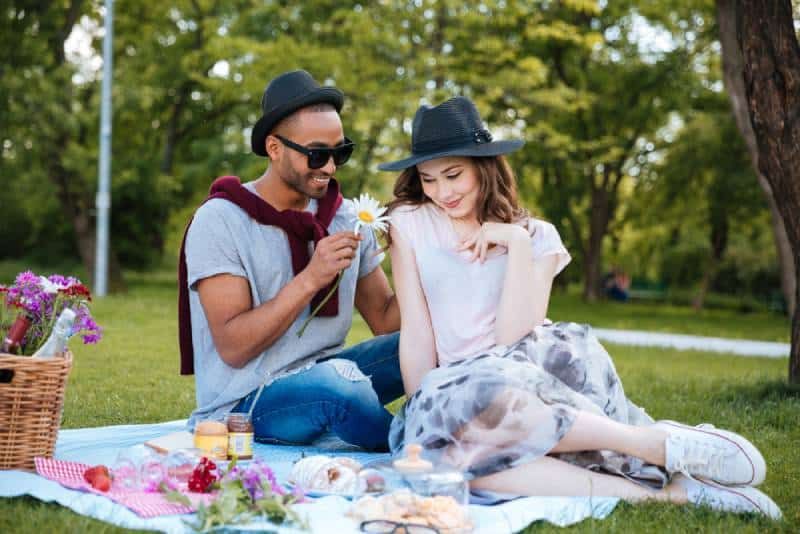 Lächelnder junger Mann, der seiner schüchternen Freundin beim Picknick Blumen schenkt