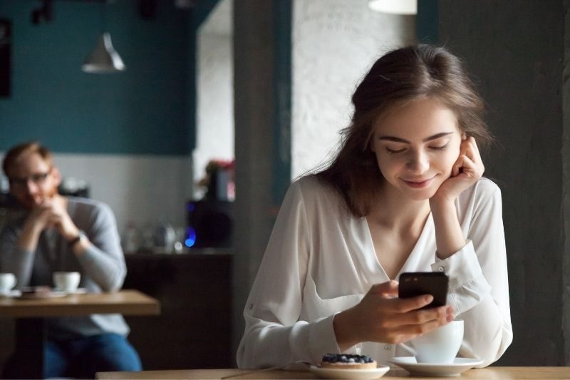 Frau liest SMS auf ihrem Smartphone im Café mit verschwommenem Hintergrund
