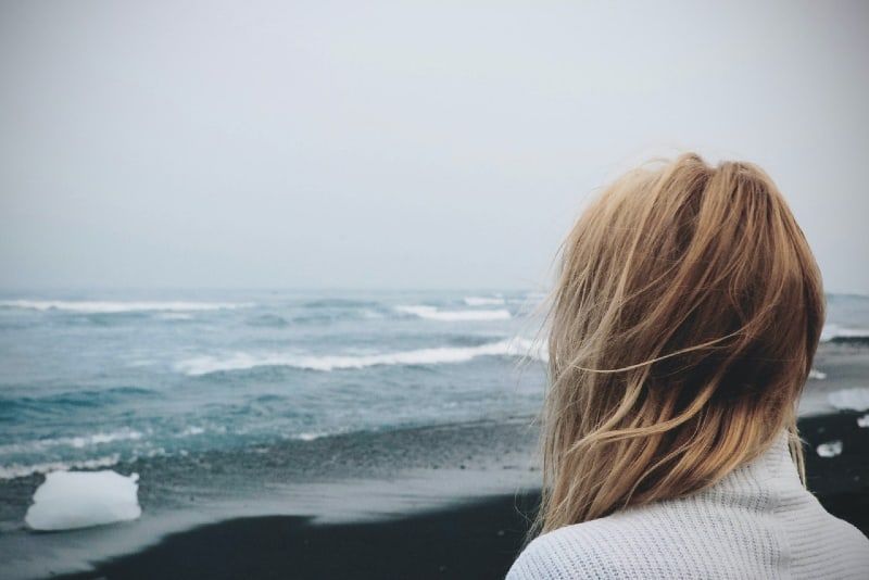 Blonde Frau im weißen Pullover mit Blick auf das Meer