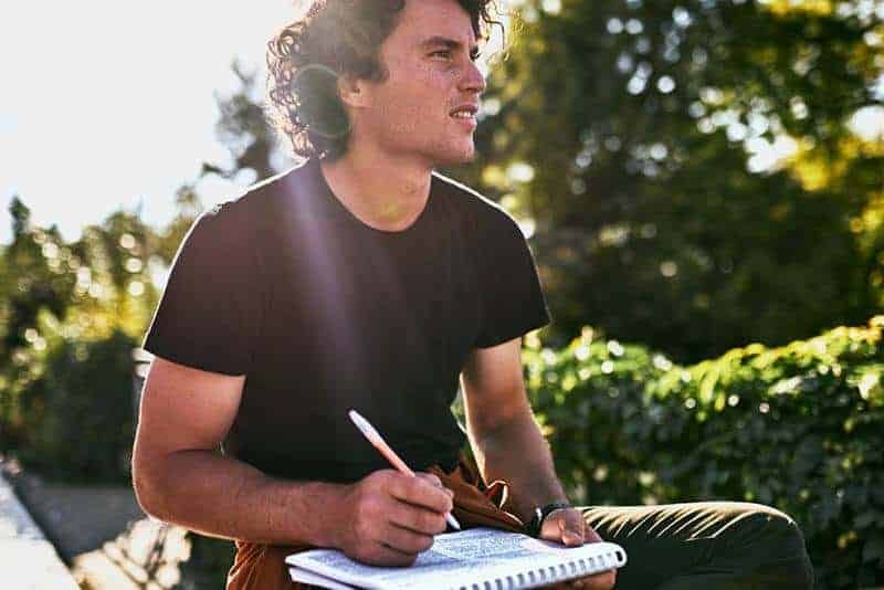 Mann schreibt draußen mit Stift auf Papier