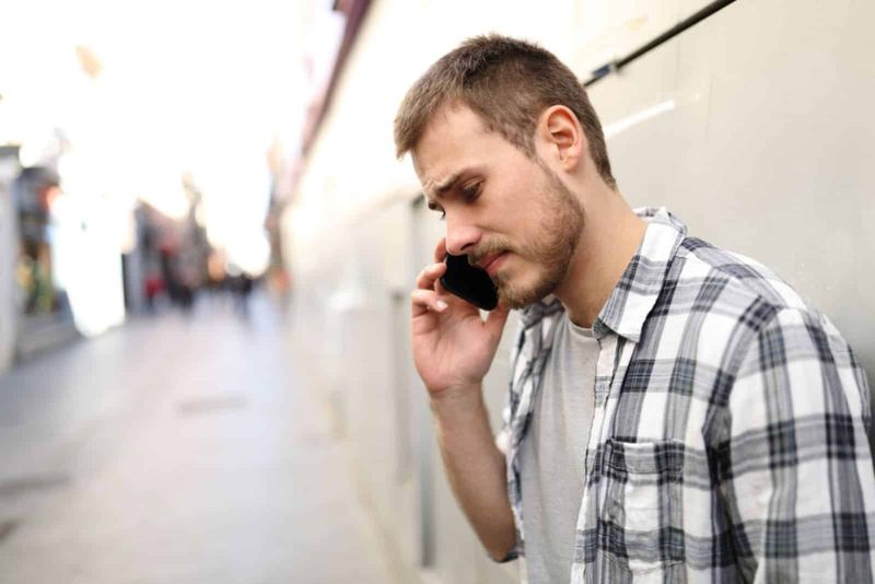 Trauriger Mann, der allein in einer einsamen Straße telefoniert
