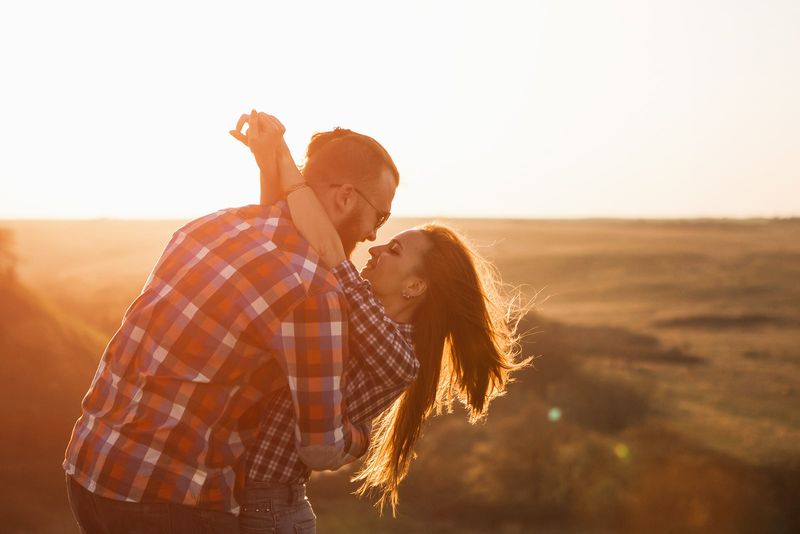 Ein Mann und eine Frau umarmen und küssen sich bei Sonnenuntergang auf einem Feld
