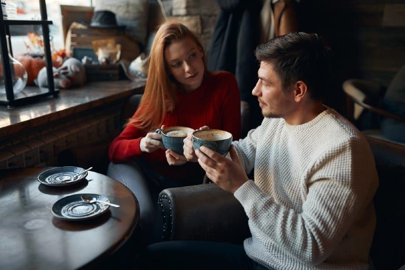Frau im roten Pullover und Mann, die Kaffee trinken, während sie am Tisch sitzen