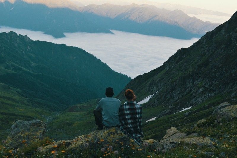 Mann und Frau sitzen auf einem Felsen und schauen auf den Berg