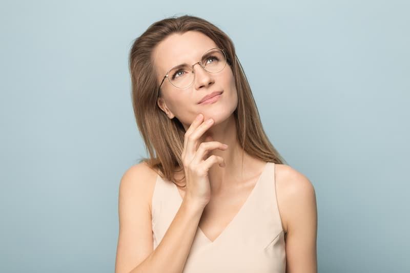 Nachdenkliche Millennial-Frau mit Brille, die nach oben schaut