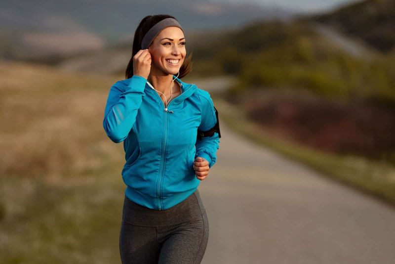 Eine lächelnde Frau mit Kopfhörern auf den Ohren rennt