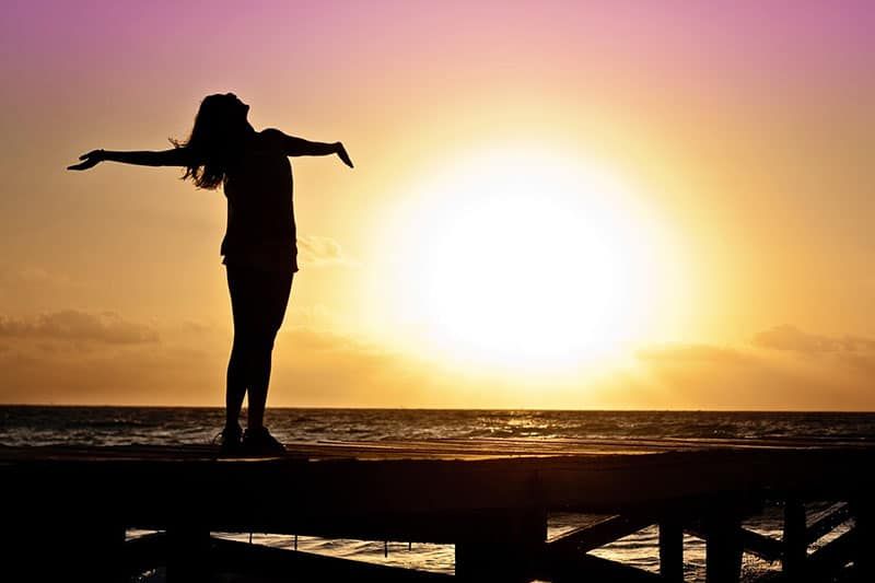 Frau am Strand bei einem Sonnenuntergang mit erhobenen Armen