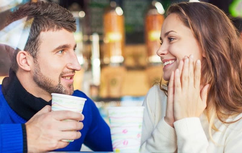 Ein Paar kommuniziert im Café mit einem Mann, der eine Tasse hält, und eine Frau kichert