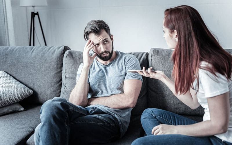 Paar streitet sich auf Sofa, während Frau ein Handy hält