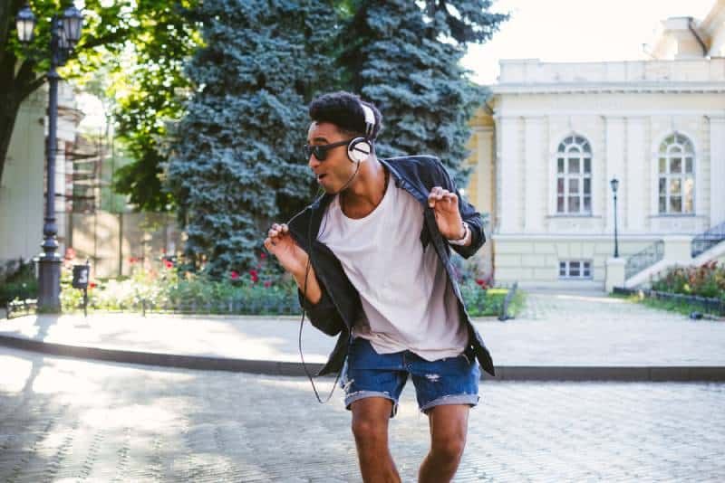 Hipster-Mann mit weißen Kopfhörern und Sonnenbrille tanzt im Freien