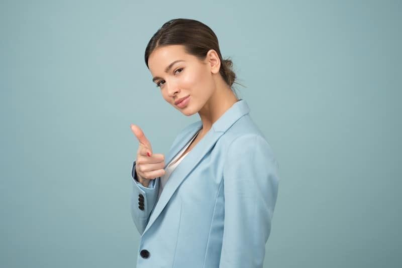 Frau zeigt mit dem Finger und trägt eine blaue Anzugjacke mit Schalrevers