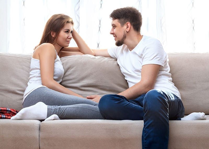 Mann und junge Frau sitzen auf einer Couch und unterhalten sich.