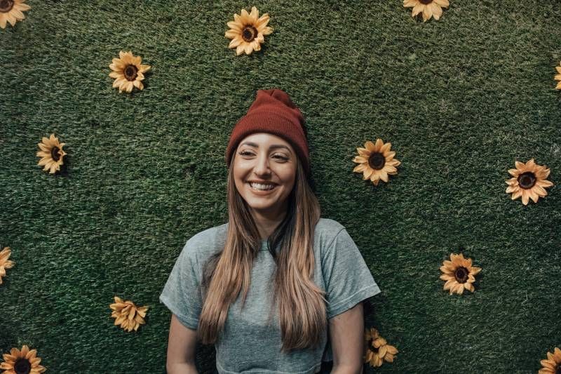Lächelnde Frau, die sich an eine Blumenwand lehnt