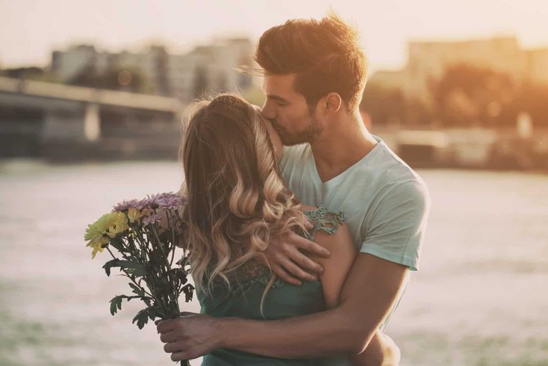 Mann hält Blumenstrauß und küsst Frau