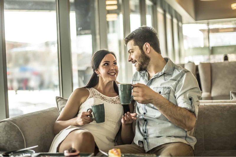 Ein lächelnder Mann und eine lächelnde Frau sitzen auf der Couch, trinken Kaffee und unterhalten sich