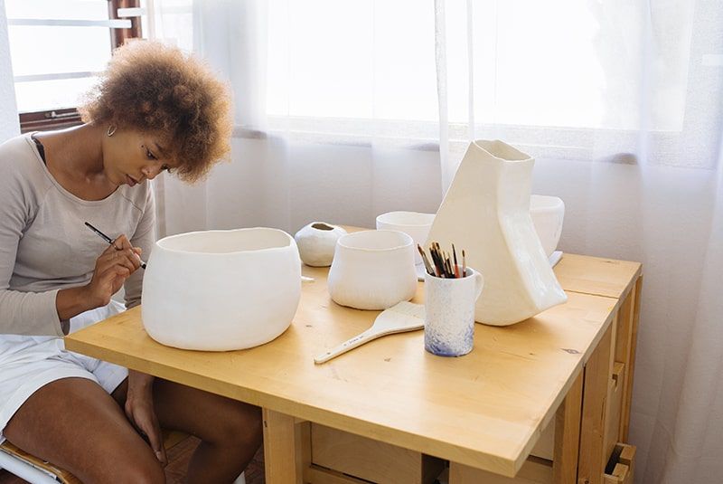 Frau bemalt Keramikschale, während sie neben dem Tisch sitzt