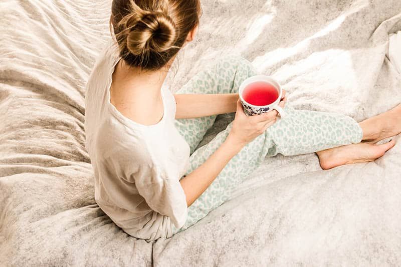 junge Frau beim Teetrinken im Bett