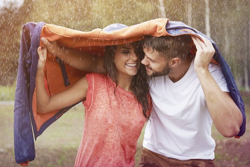 romantisches paar versteckt sich vor dem regen unter der jacke