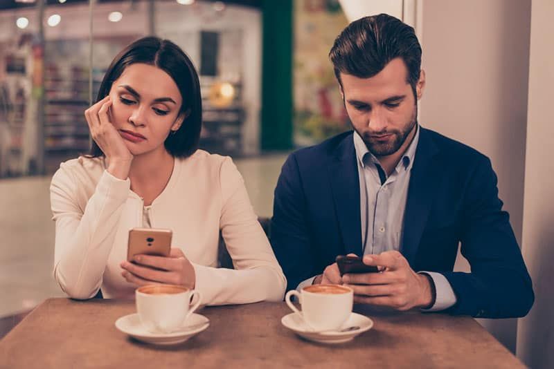 Gelangweiltes Paar sitzt in einem Café und hält Telefone in der Hand