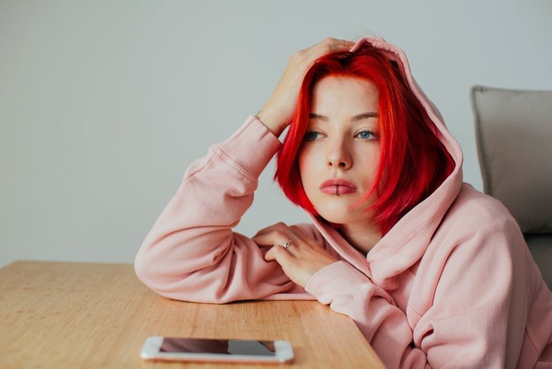 Ein trauriges rothaariges Mädchen sitzt mit einem Handy an einem Tisch