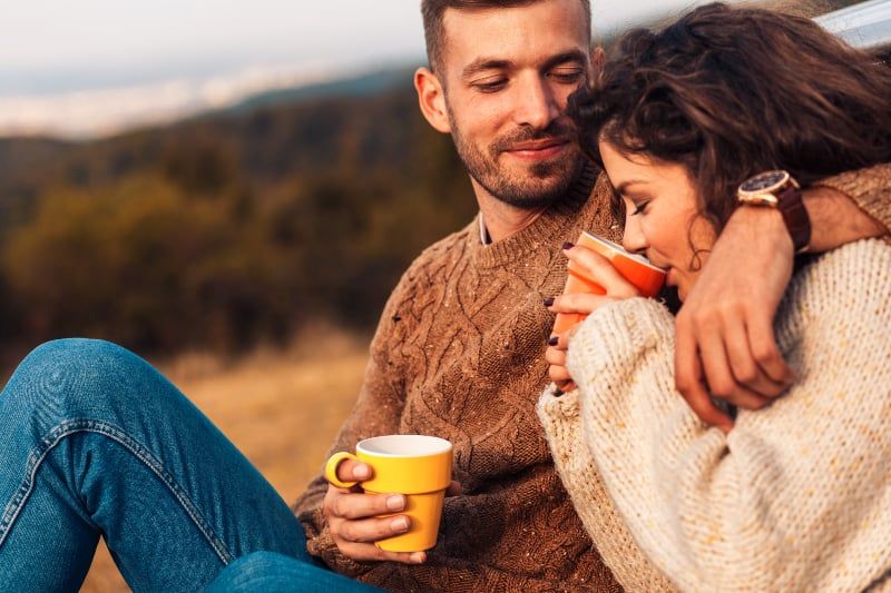 Paar im Sweatshirt trinkt draußen Kaffee