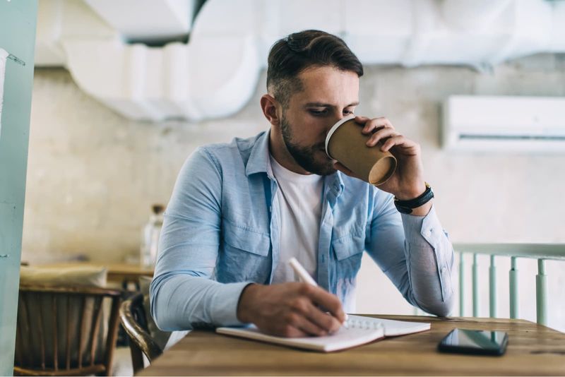 Ein Mann sitzt da, trinkt Kaffee und schreibt