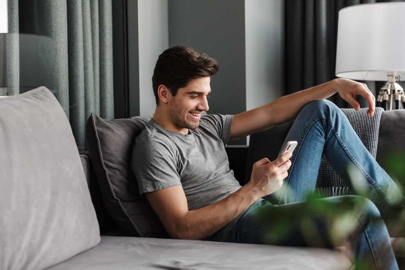 Mann sitzt auf dem Sofa und schreibt seiner Freundin eine SMS
