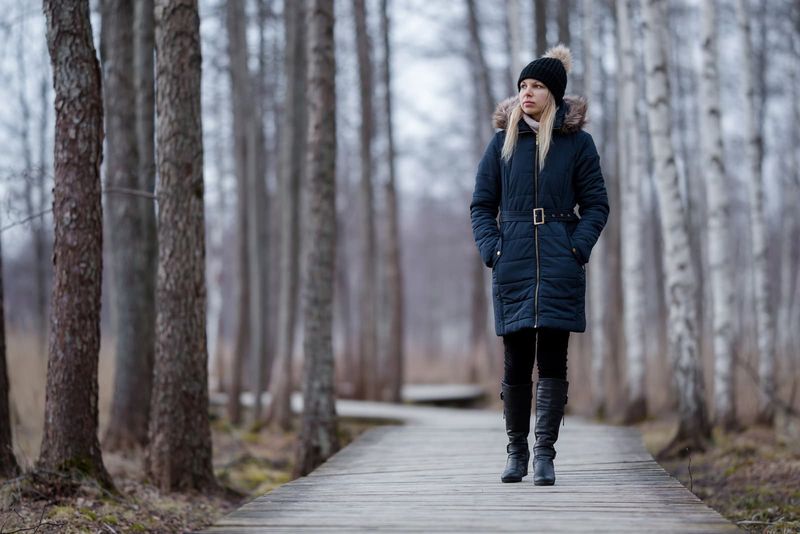 Frau in dunkler, warmer Kleidung geht langsam auf Holzweg im Naturpark