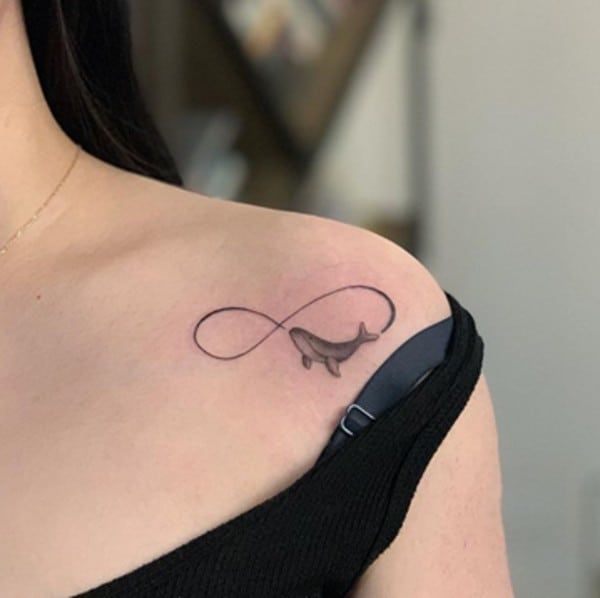 Unendlichkeitssymbol mit einem fliegenden Wal unter dem Schlüsselbein-Tattoo