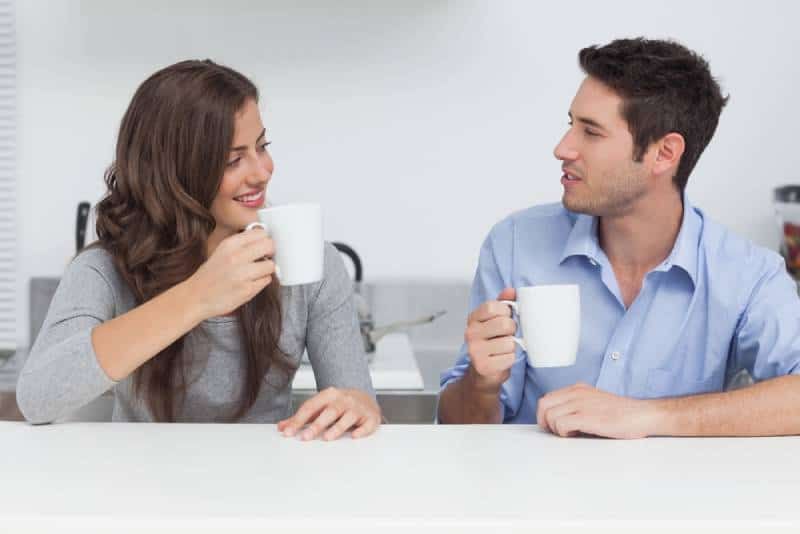 Mann und Frau unterhalten sich und halten zu Hause eine weiße Tasse Tee in der Hand