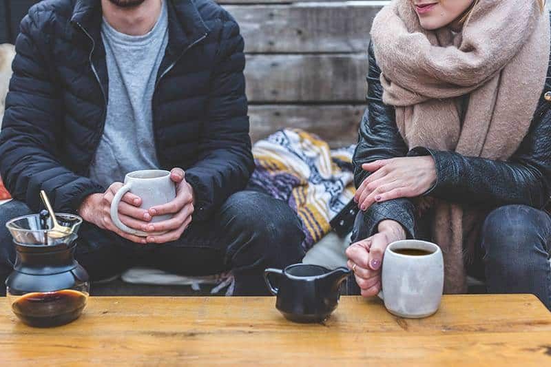 Paar trägt Jacke und hält Tasse Tee im Café