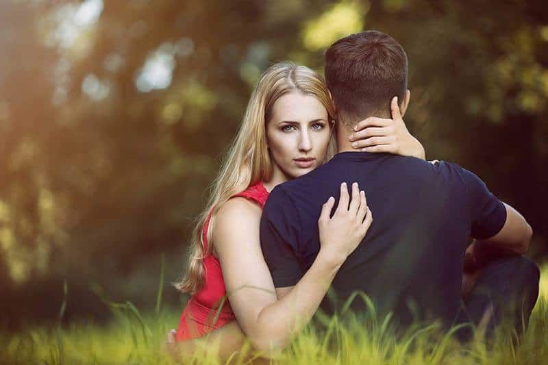 Blonde ernste Frau umarmt Mann auf dem Rasen