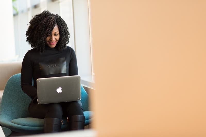 Eine lächelnde schwarze Frau sitzt und benutzt einen Laptop