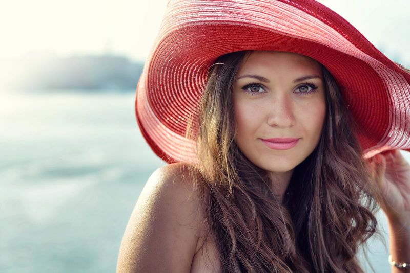 Schönes Mädchen mit rotem Hut, das im Sommer am Wasser lächelt