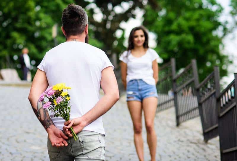Mann hält Blumen in der Hand und wartet auf seine Freundin