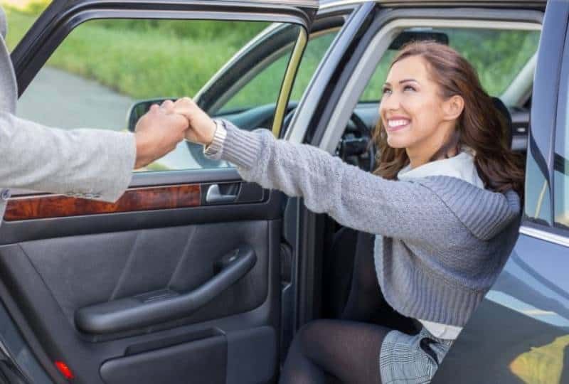 Mann hält lächelnde Frau an der Hand, während sie aus dem Auto steigt