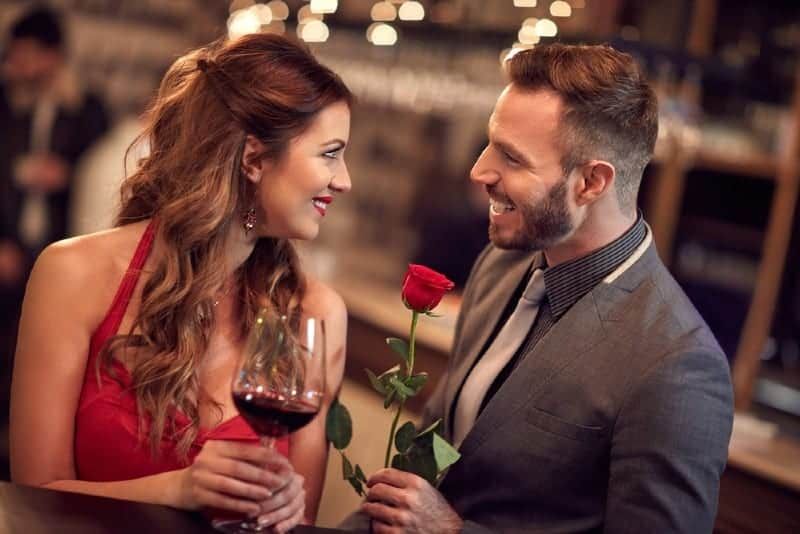 Ein Mann mit Rosen steht vor einer Frau, die ein Glas hält und einander ansieht