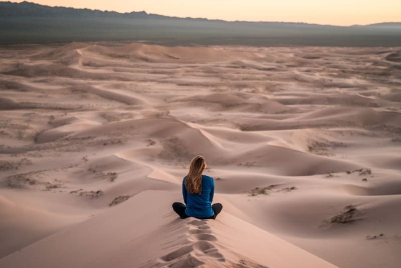 Frau im blauen Oberteil sitzt auf einem Sandfeld