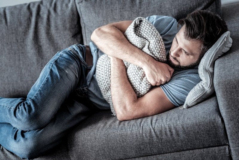 Depressiver Mann umarmt Kissen, während er zu Hause auf der Couch liegt