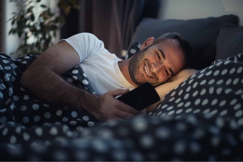 glückliche Männer, die im Bett liegen und SMS schreiben
