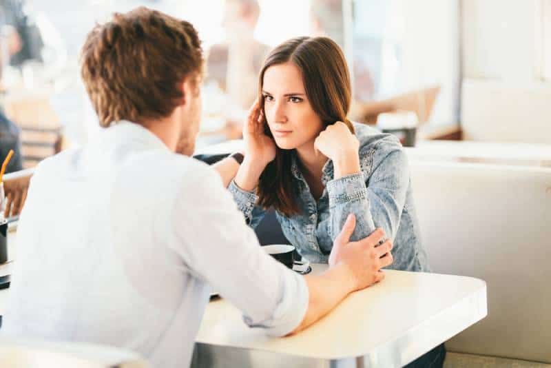 Frau schaut Mann misstrauisch an, während er ihre Arme im Café hält