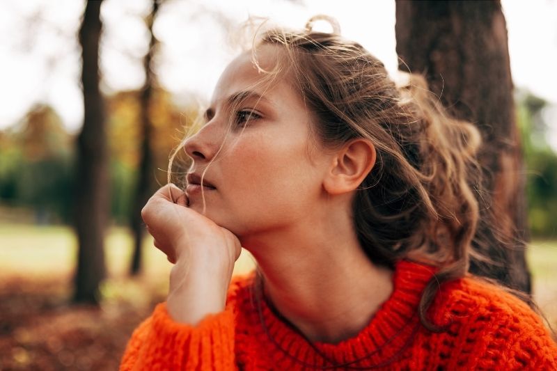 Frau im orangefarbenen Pullover denkt tief nach, während sie draußen sitzt