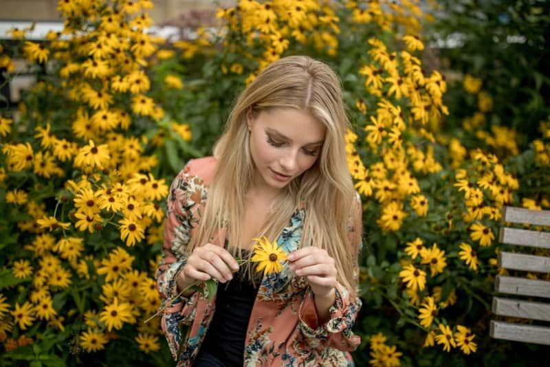 Frau, die gelbe Blume hält, während sie im Freien steht