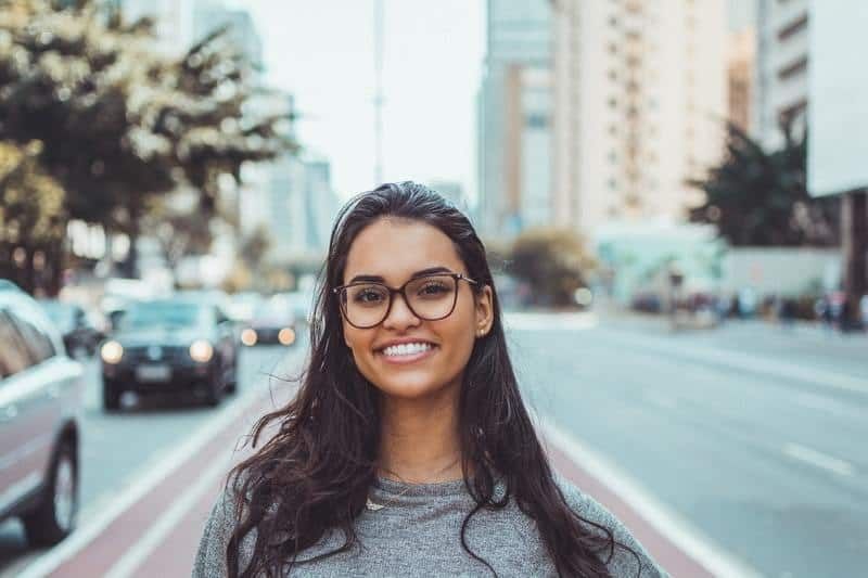 schöne junge lächelnde Frau, die auf der Straße steht und eine Brille trägt