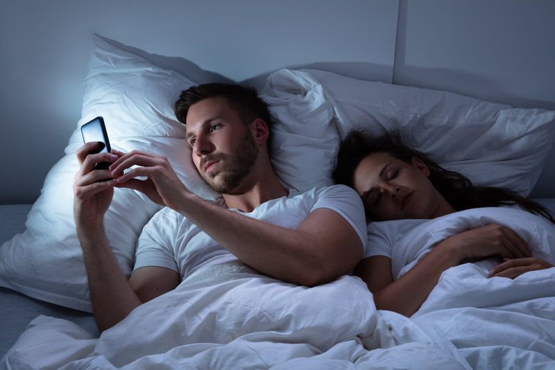 Mann tippt im Bett, während Frau schläft
