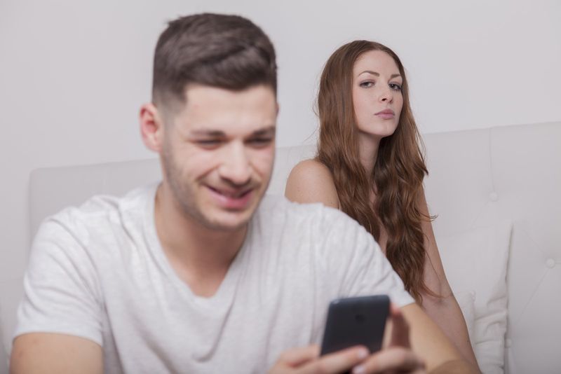 Eifersüchtige Frau, die Mann beim SMS-Schreiben beobachtet